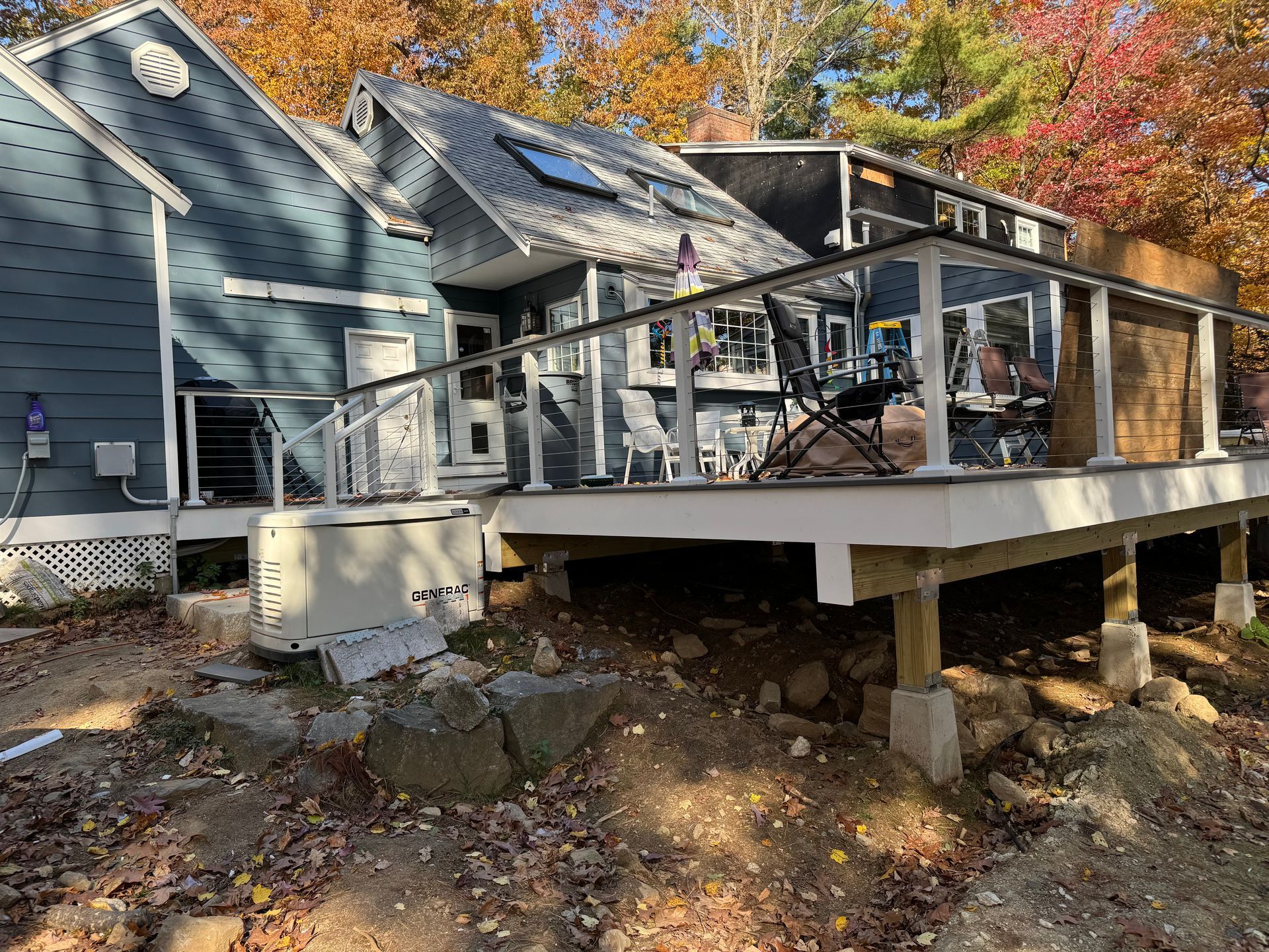 Blue house with a deck supported by posts. Rocks and fall foliage surround it.