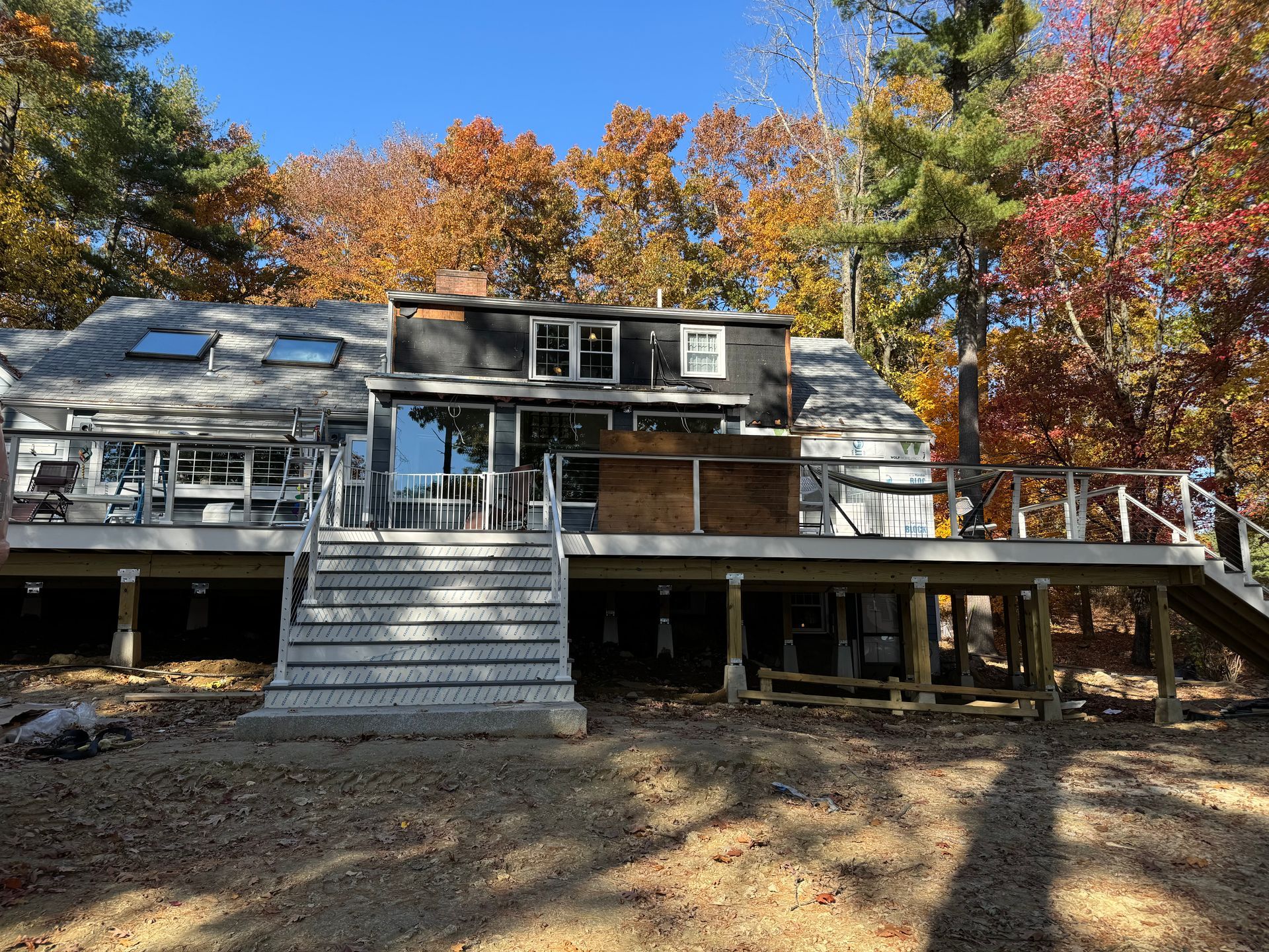A house with a large deck; autumn leaves in the background. Gray steps lead up to the deck.