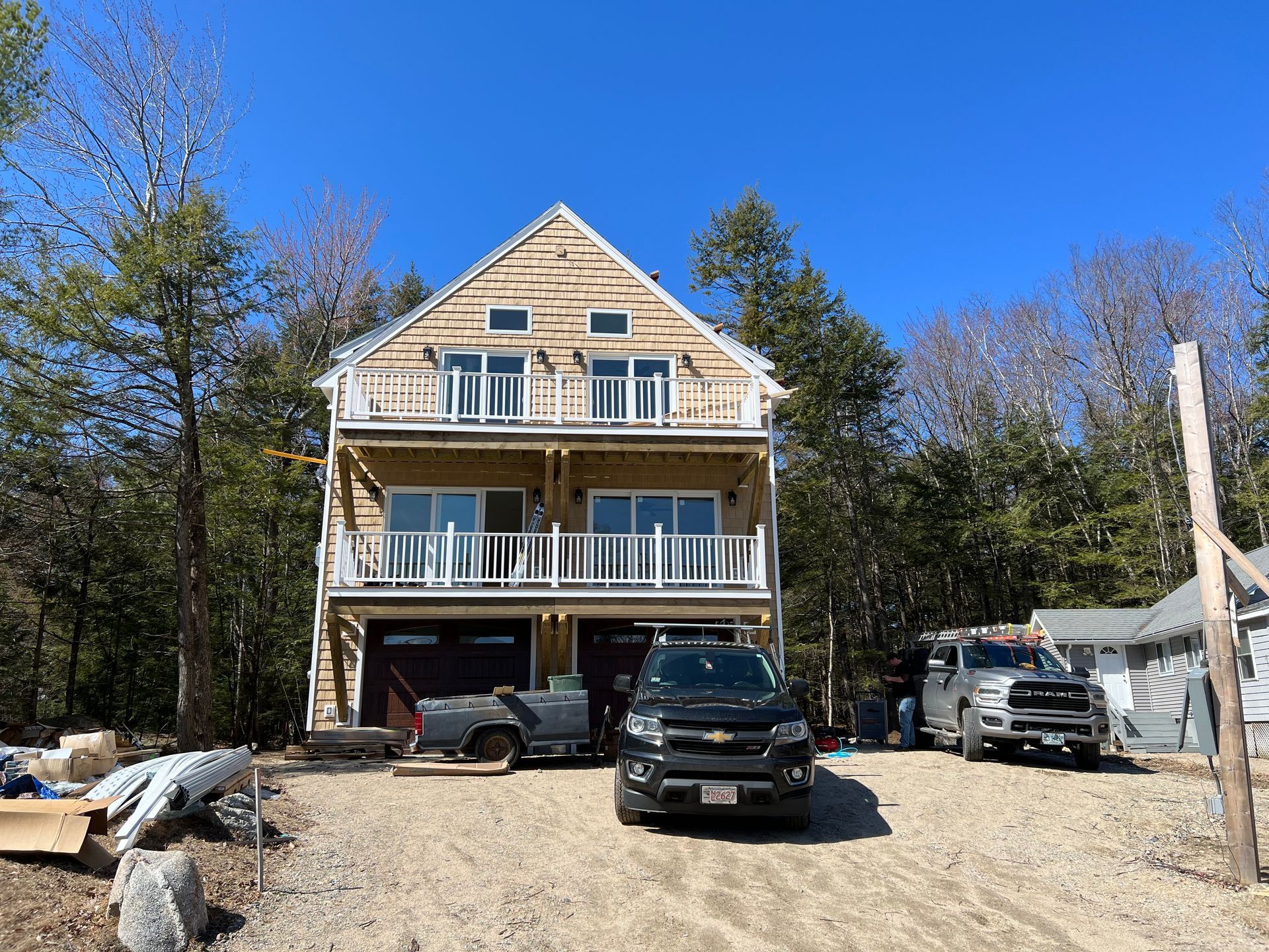 Two-story house with balconies, two garage doors, and vehicles parked in front. Sunny day.