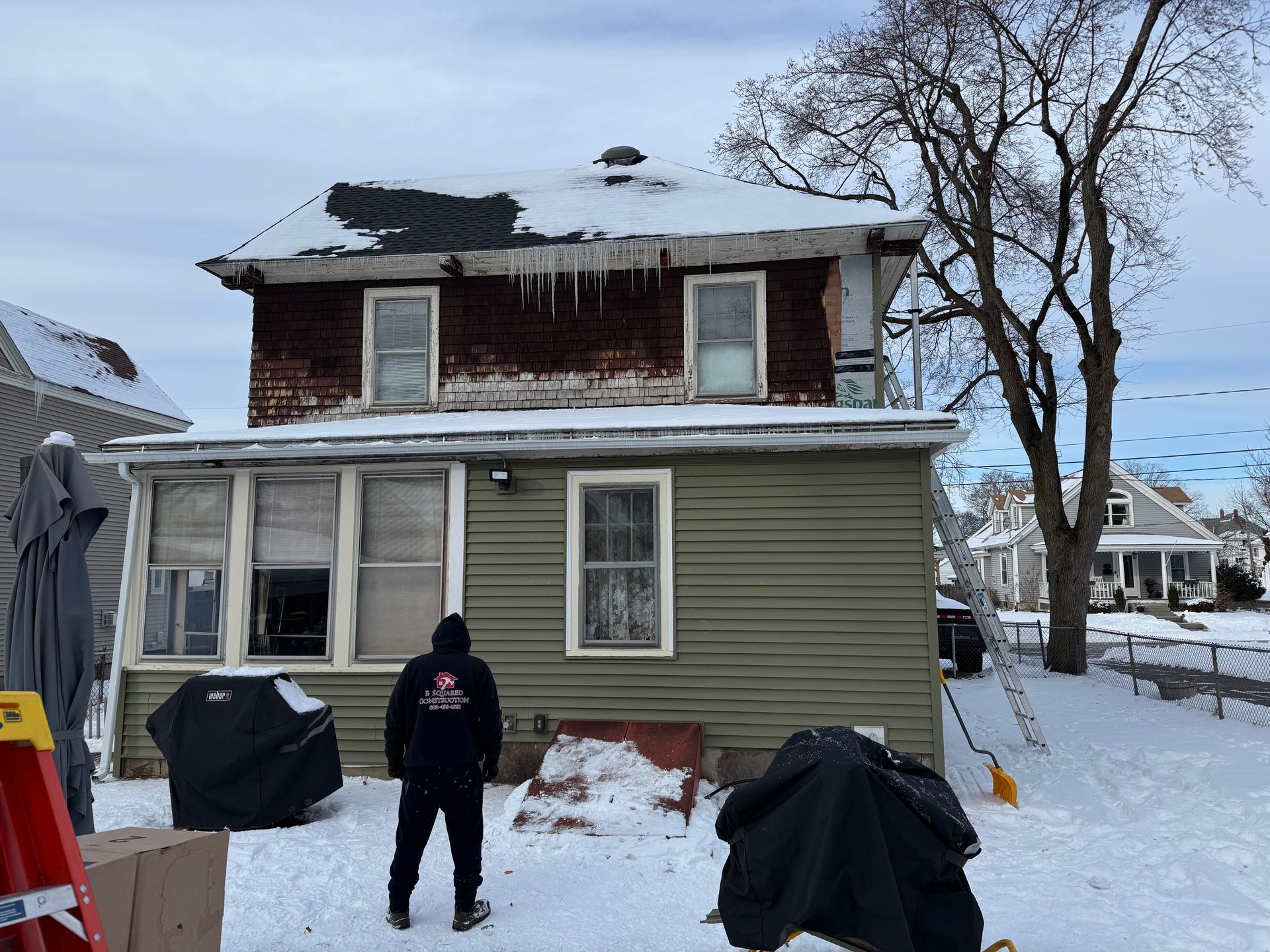 Back view of a two-story house with icicles, snow, and a person in black clothing.