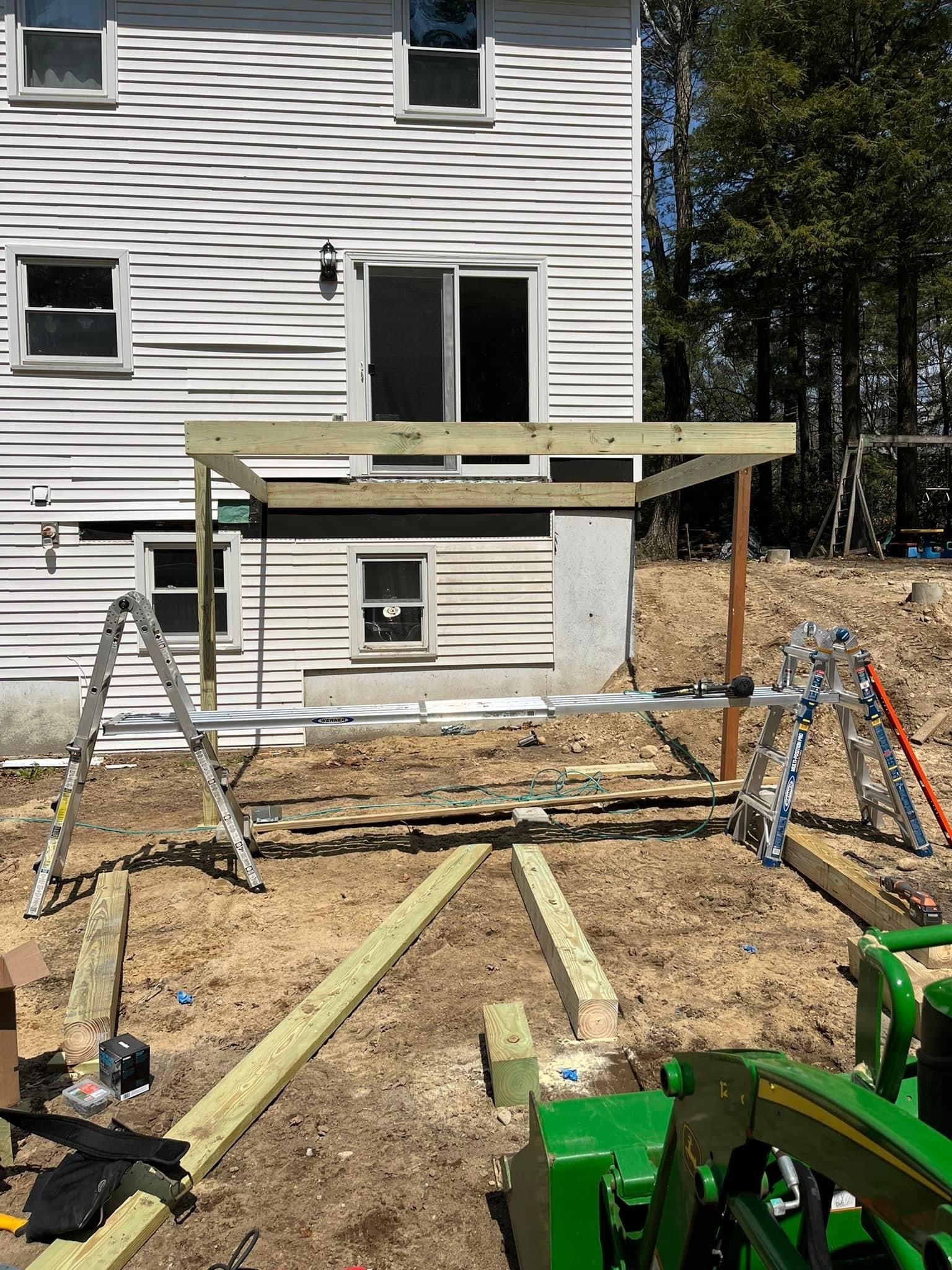 Construction of a wooden deck attached to a white house. Green tractor and ladders are nearby.