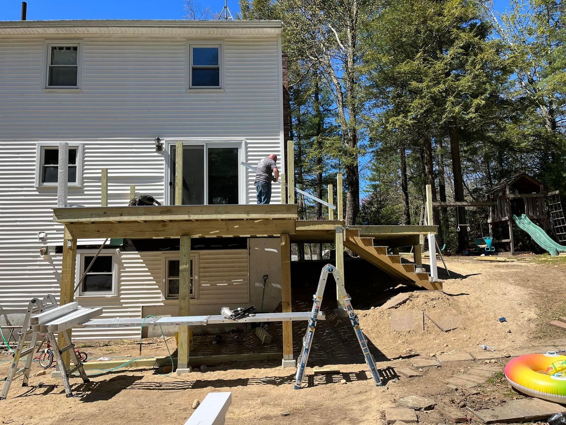 Deck construction in progress at a house. A worker is standing on the deck. Sunny day.