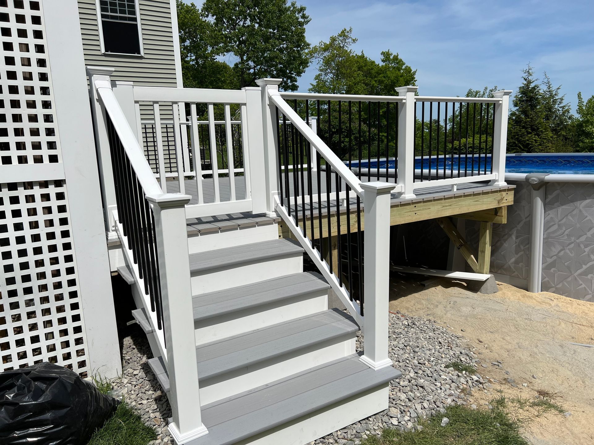 A deck with gray steps and white railing leads to an above-ground pool.
