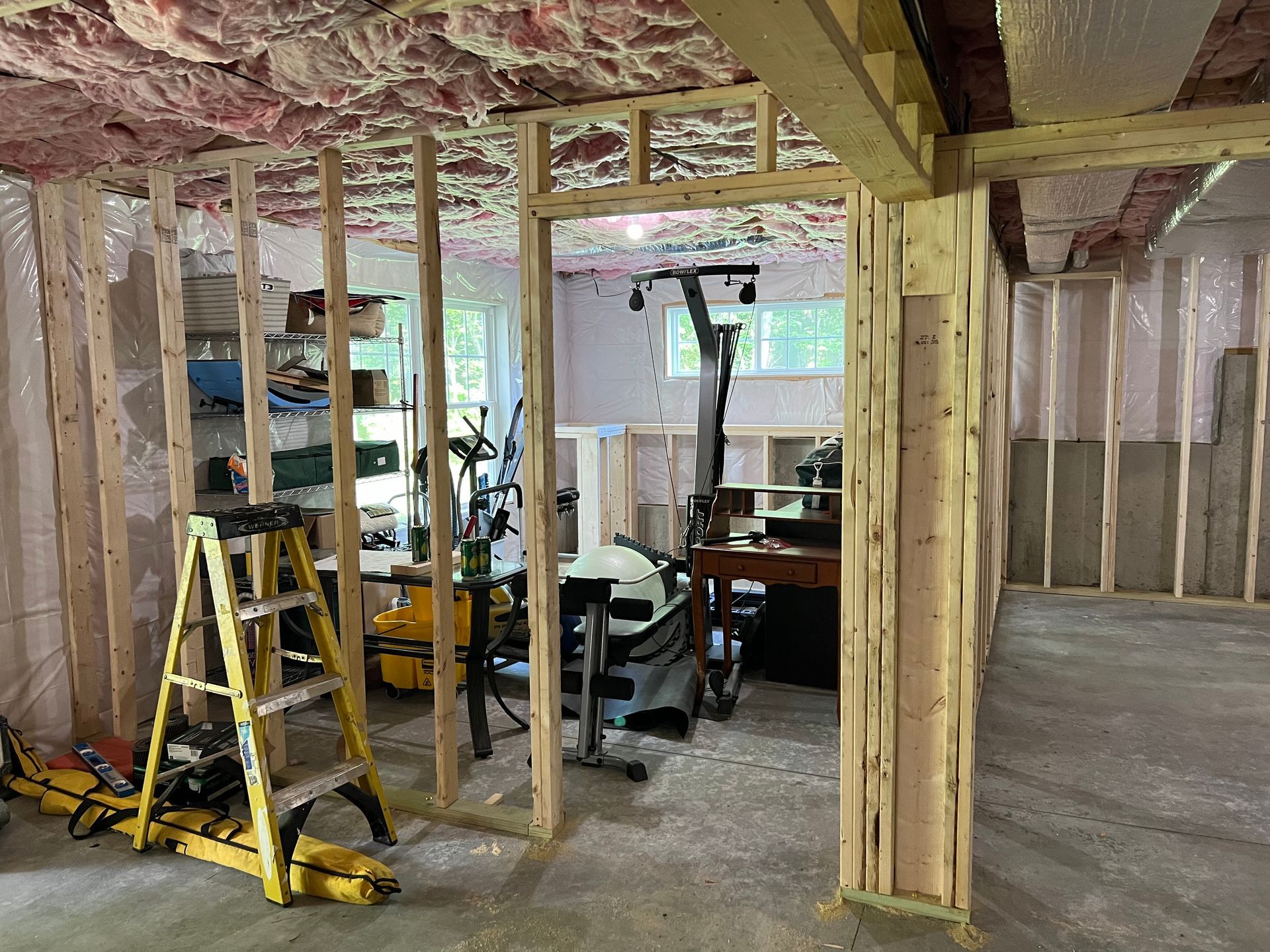 Basement under construction, framed walls with insulation, doorway to a room with exercise equipment.