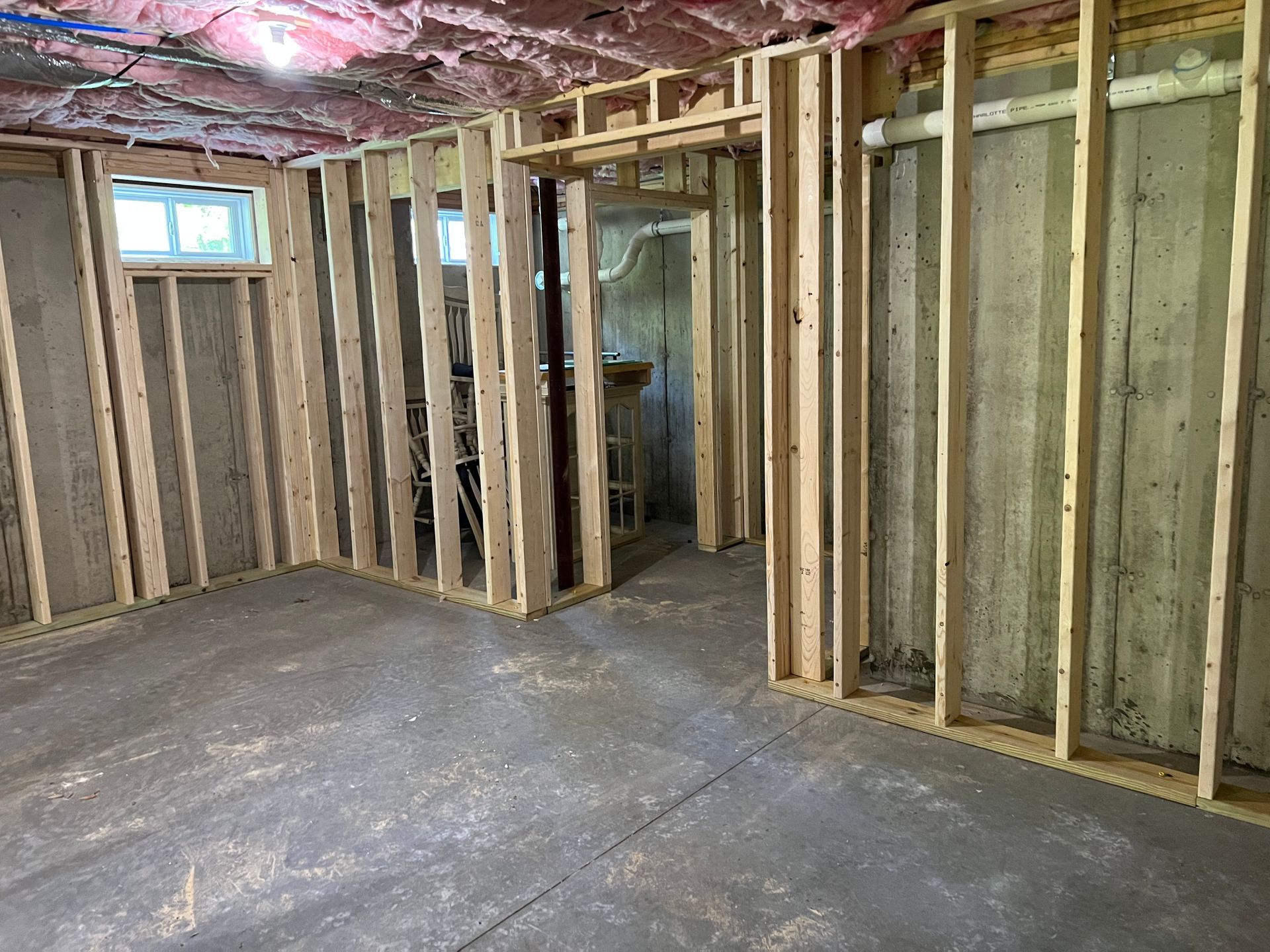 Basement framing: studs, doorway, concrete floor, unfinished walls, pink insulation on ceiling.