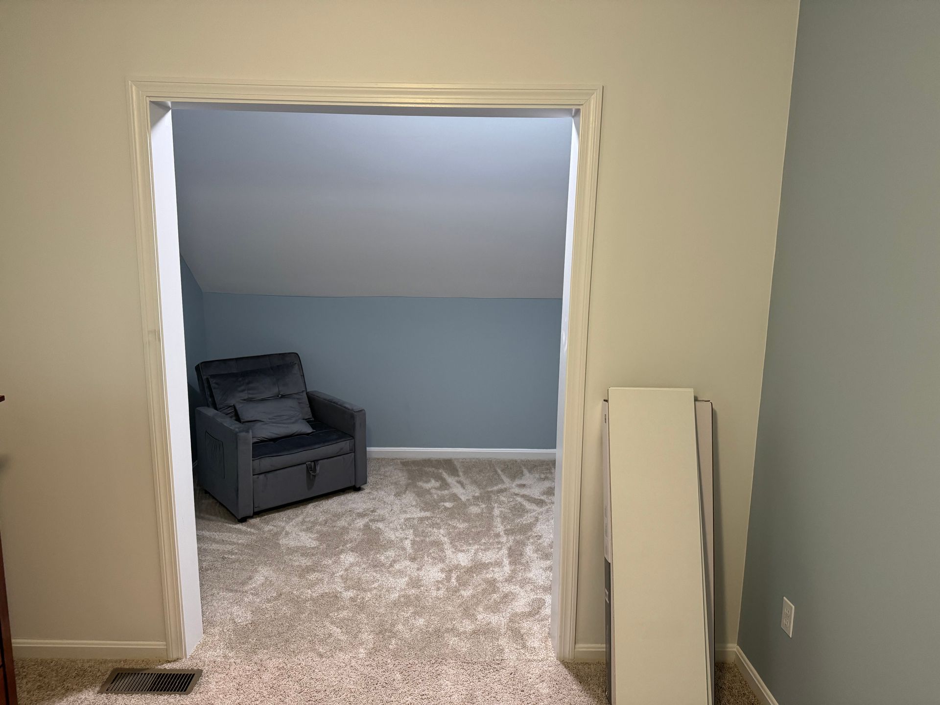 A doorway leads into a room with a blue wall, gray chair, and beige carpet.