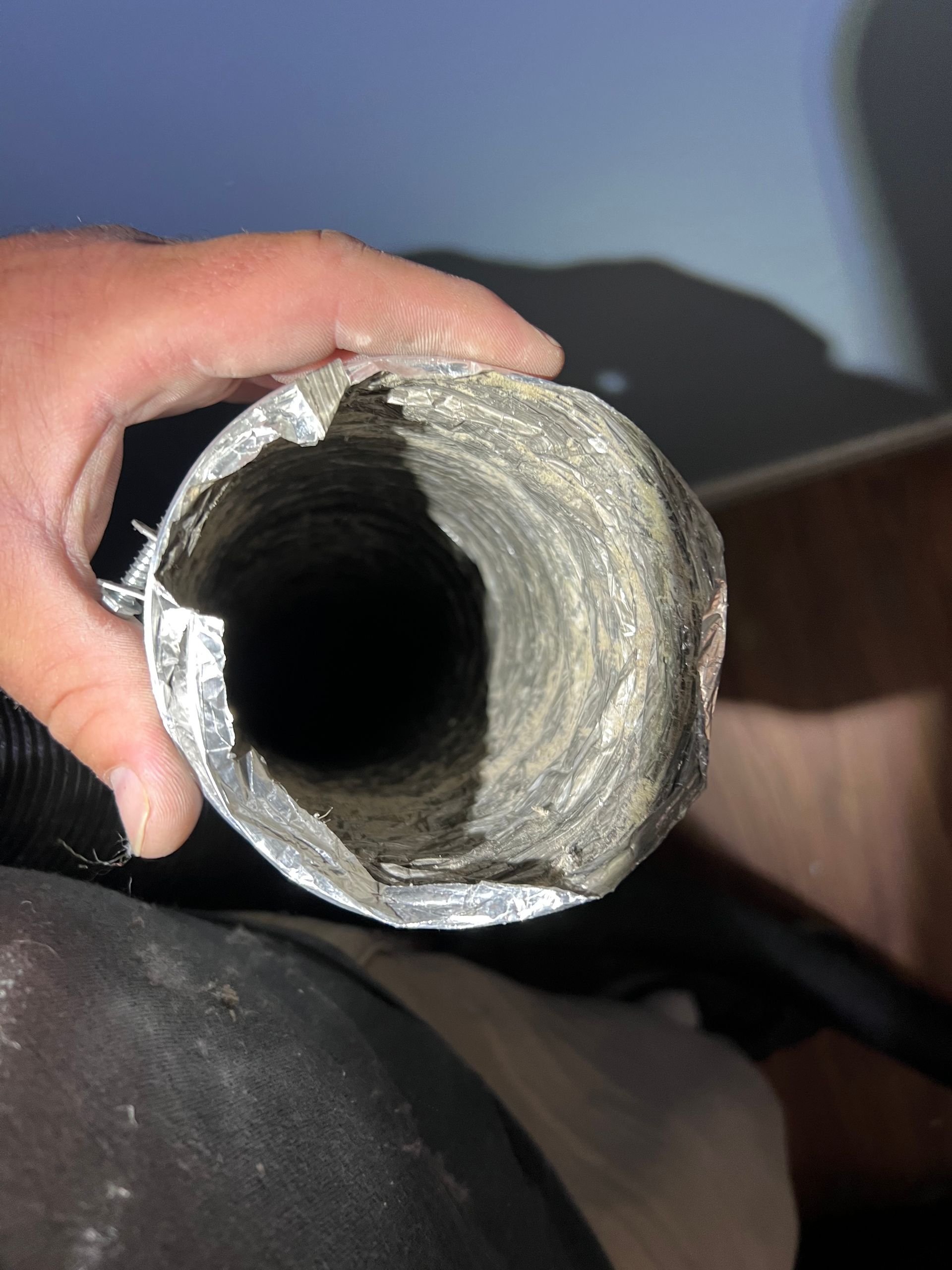 Hand holding a dirty, damaged, flexible dryer vent.