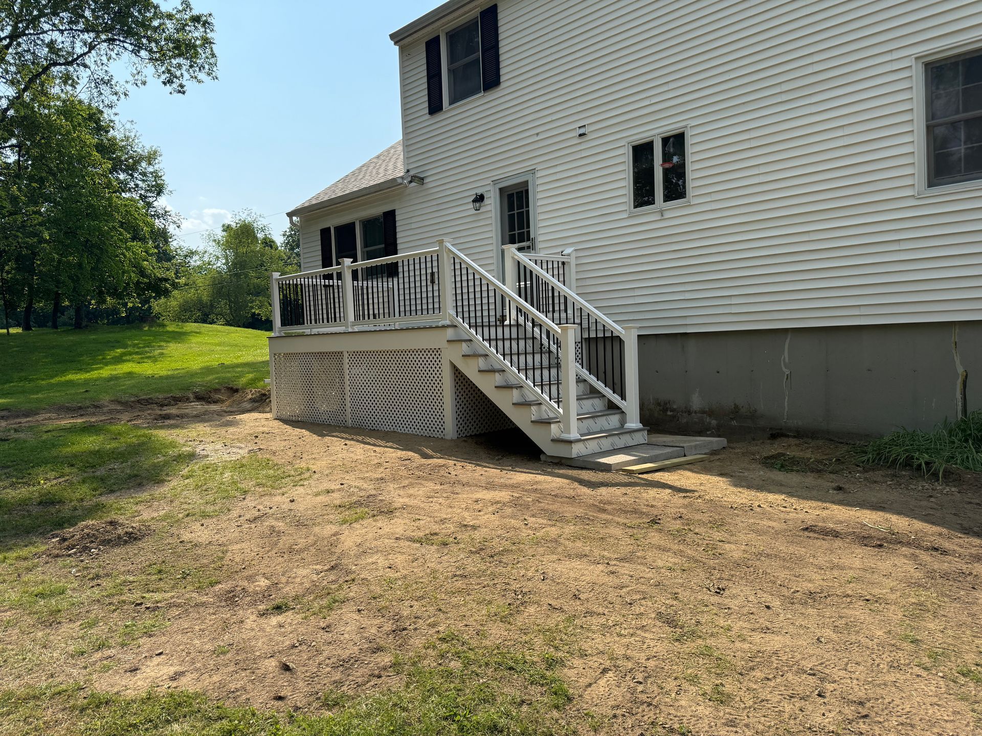 White house with deck and stairs leading to a yard, on a sunny day.