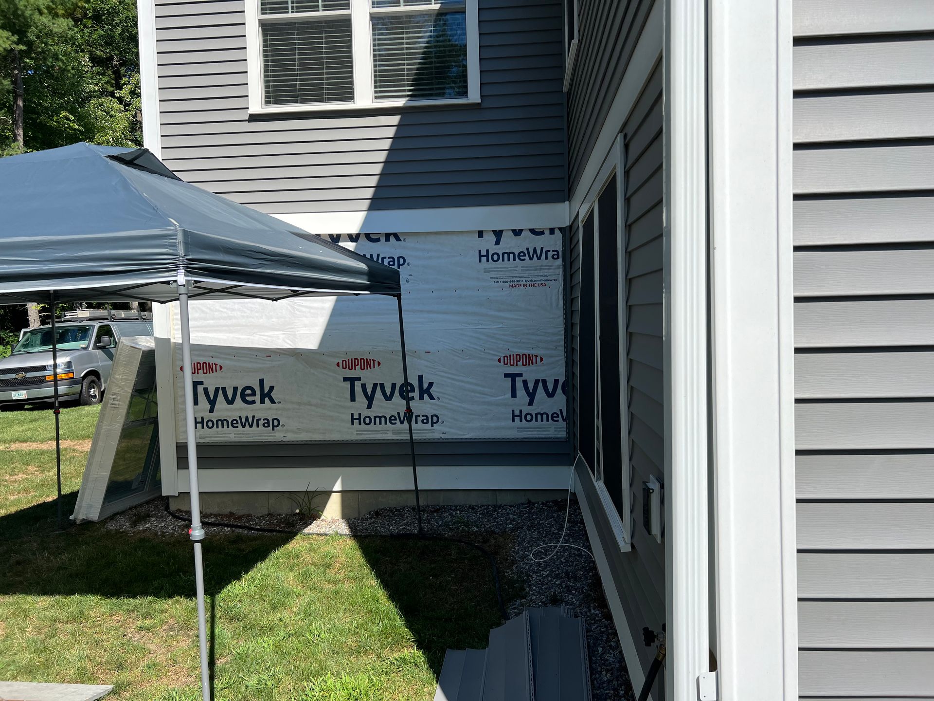 Gray house exterior under construction, partially covered with Tyvek wrap, a tent, and window.