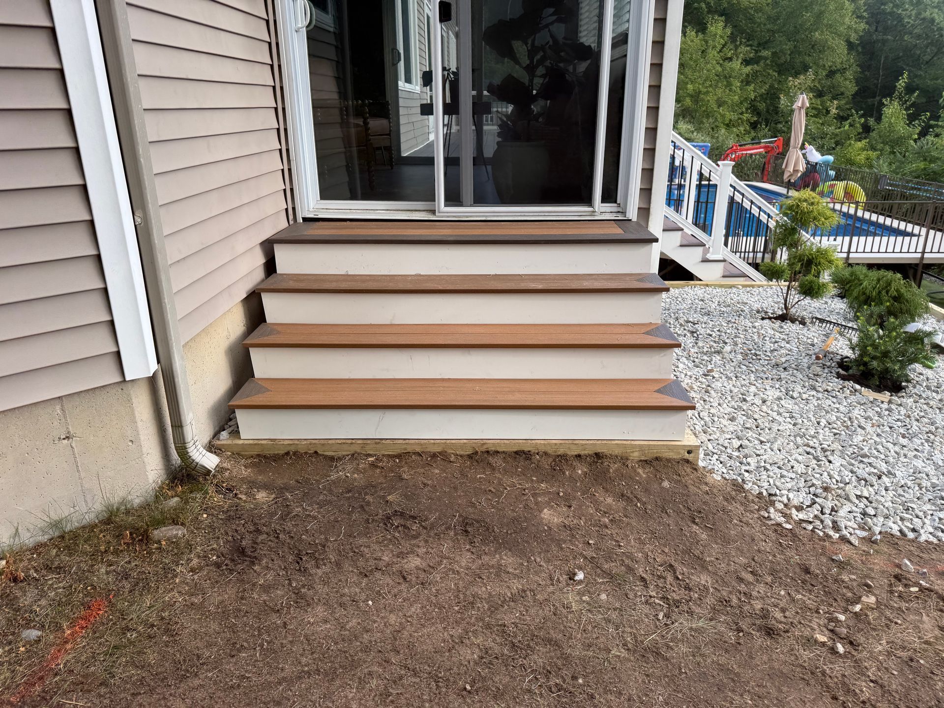 Wooden steps leading up to a sliding glass door. Steps are light brown with white trim, outside a tan house.
