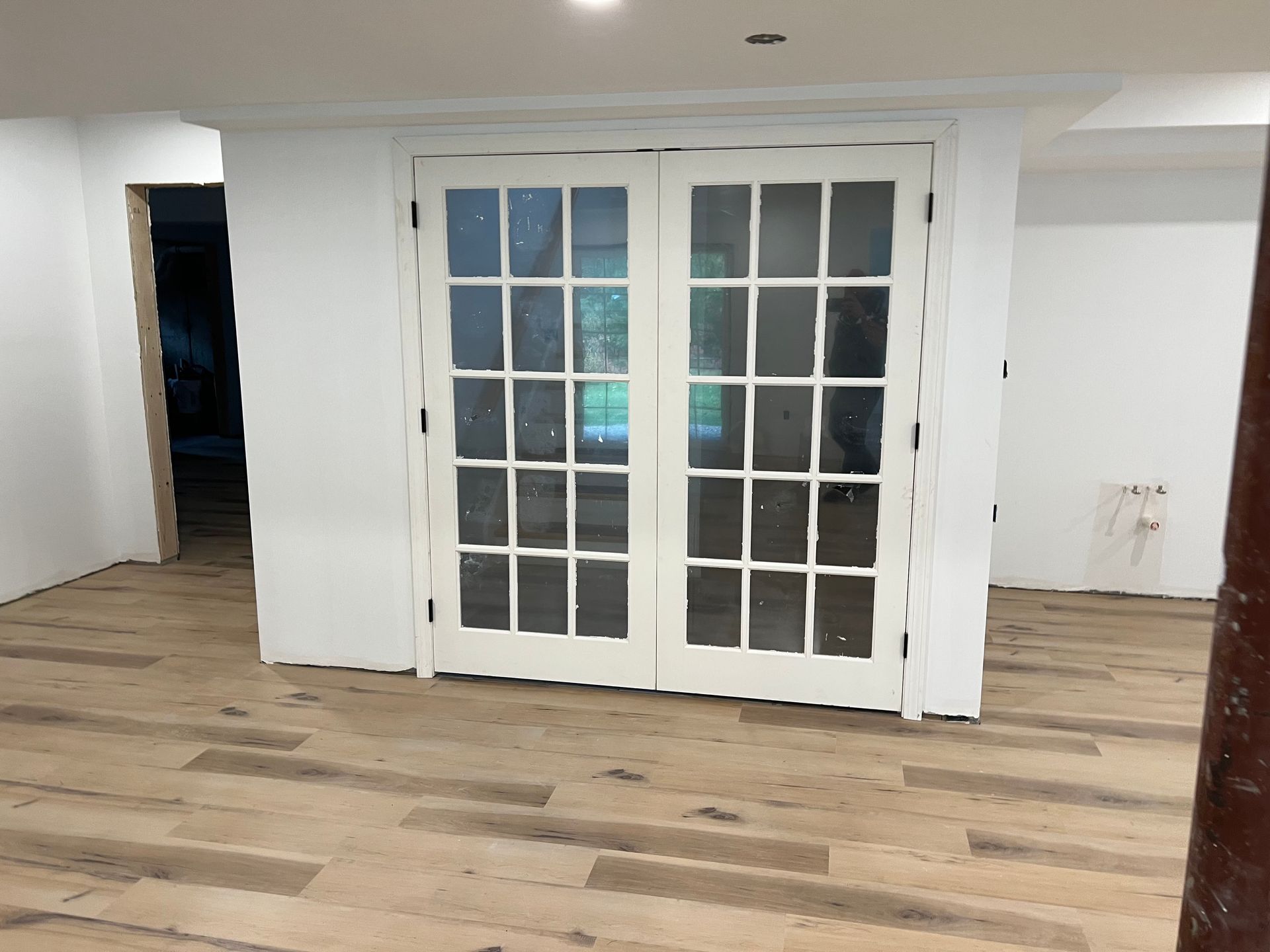 White French doors in a room with wood flooring, painted white walls, and a view into another room.