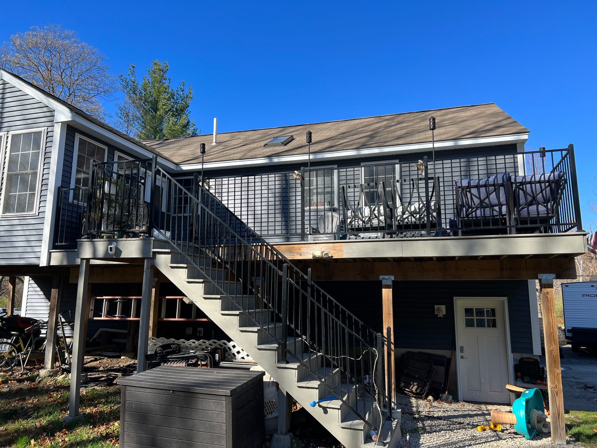 Two-story house with stairs leading to a deck. Blue siding and a white door. Clear, sunny sky.