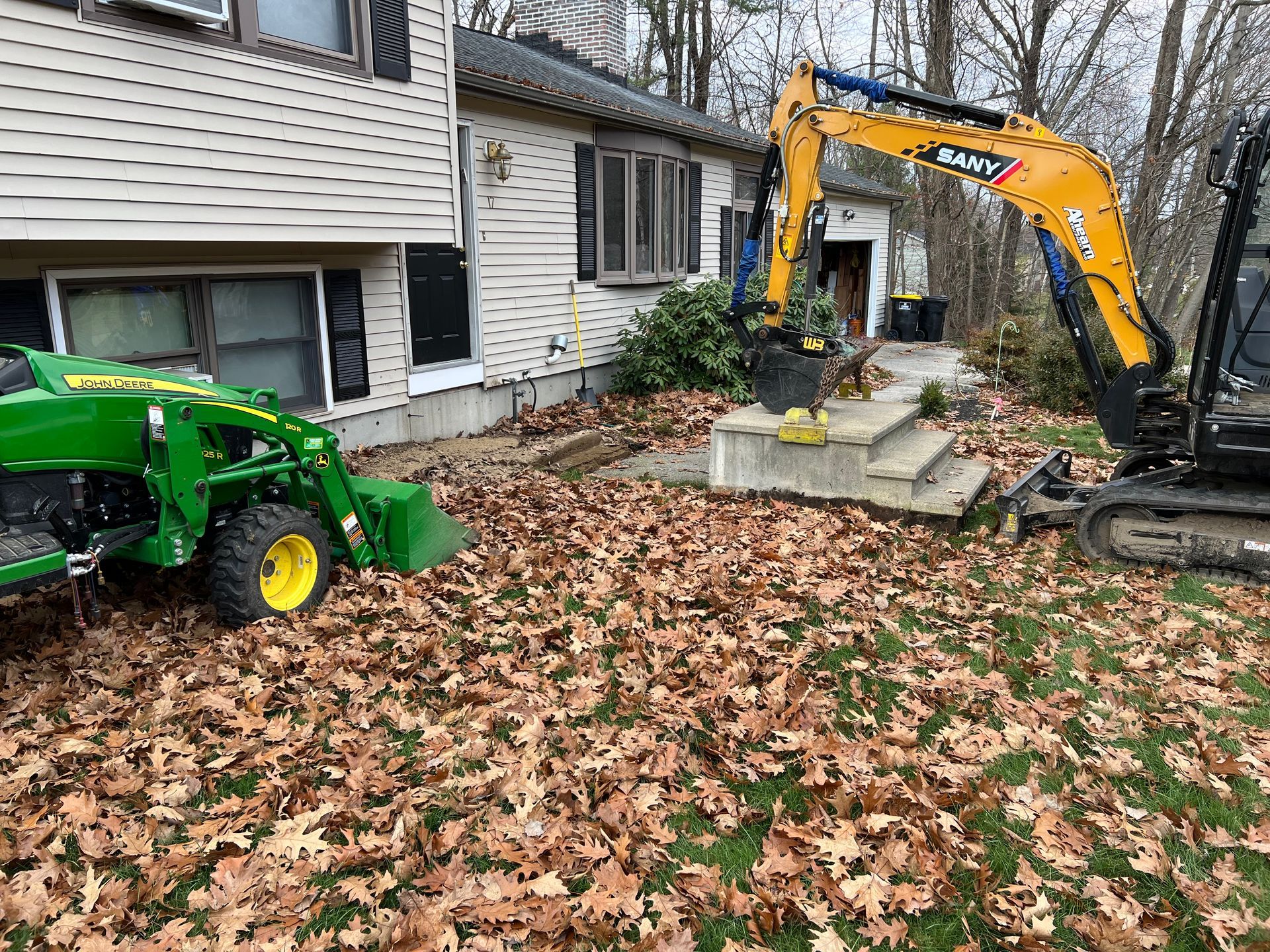 Construction equipment next to a house with steps; a John Deere tractor and an excavator are visible.