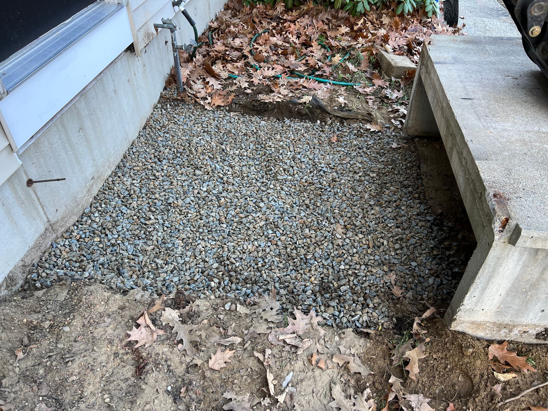 Gravel and dirt area next to a building foundation and concrete step. Brown leaves and debris in the background.