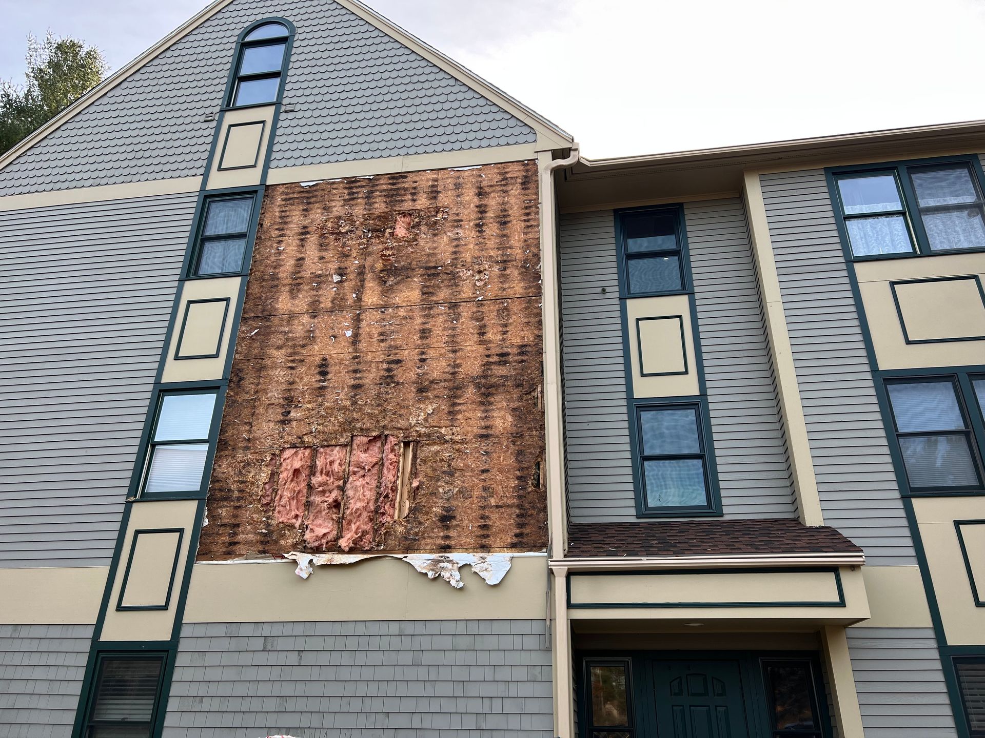 Building exterior with damaged siding, exposing weathered wood and insulation.