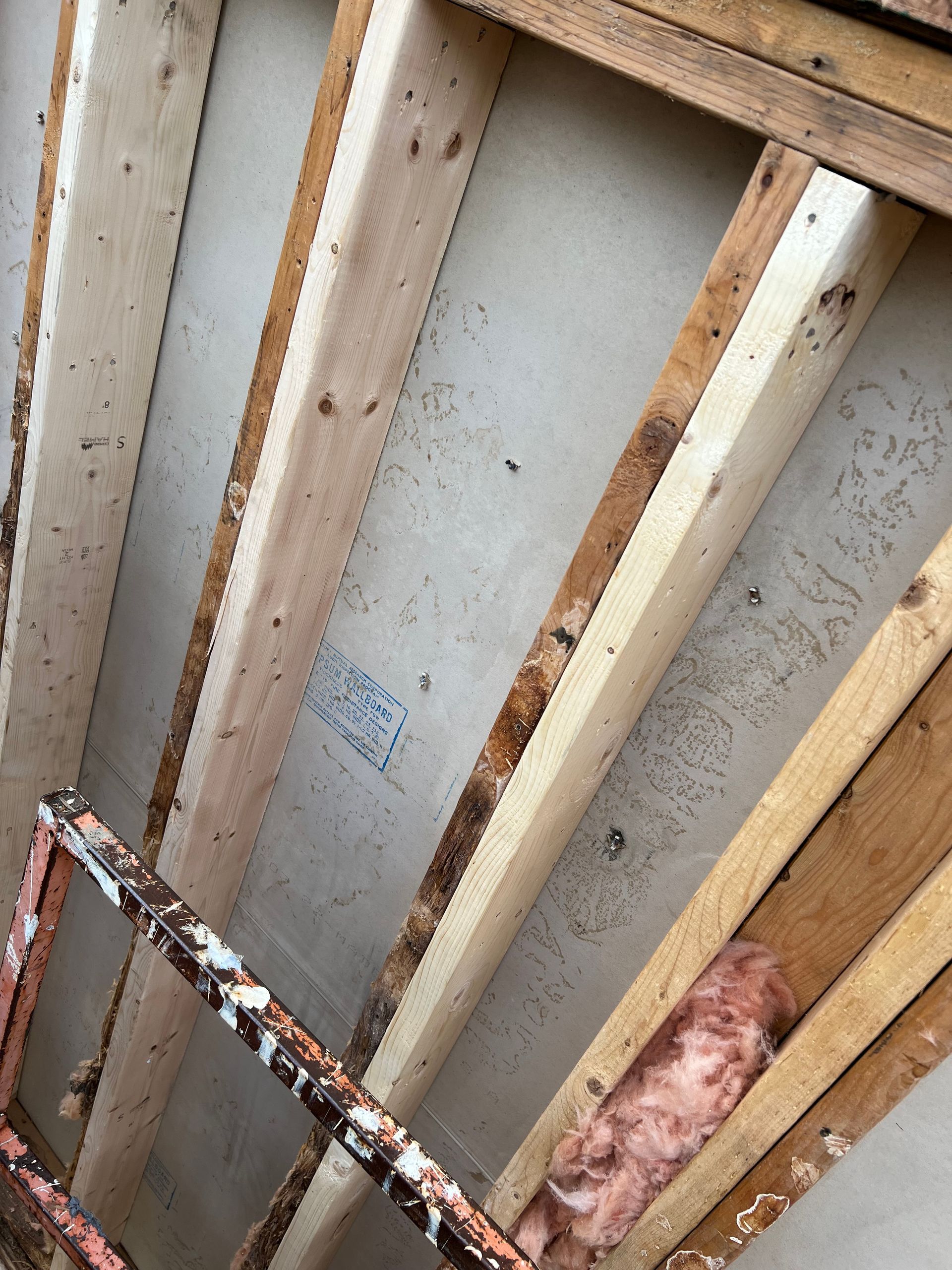 Wooden rafters and drywall show signs of water damage, rust on a nearby metal structure.