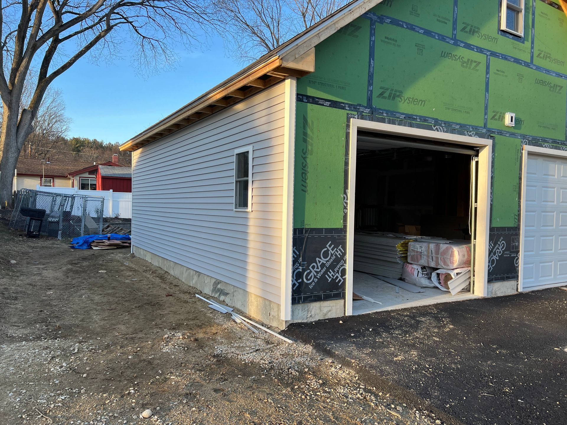 Garage under construction with gray siding, open door, and blue sky.