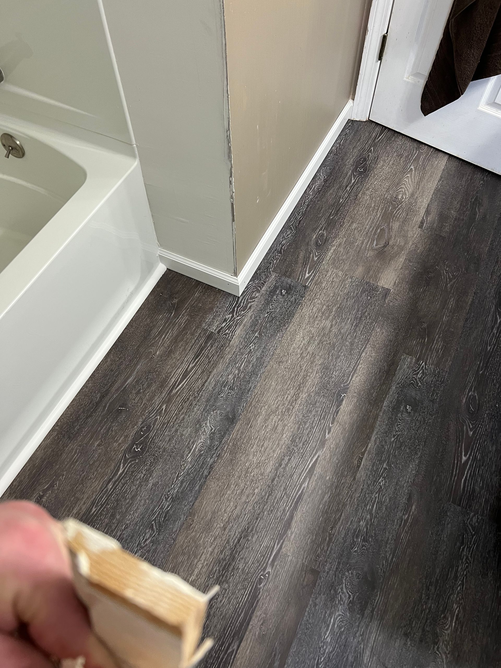 Dark brown vinyl flooring with white trim near a white tub.