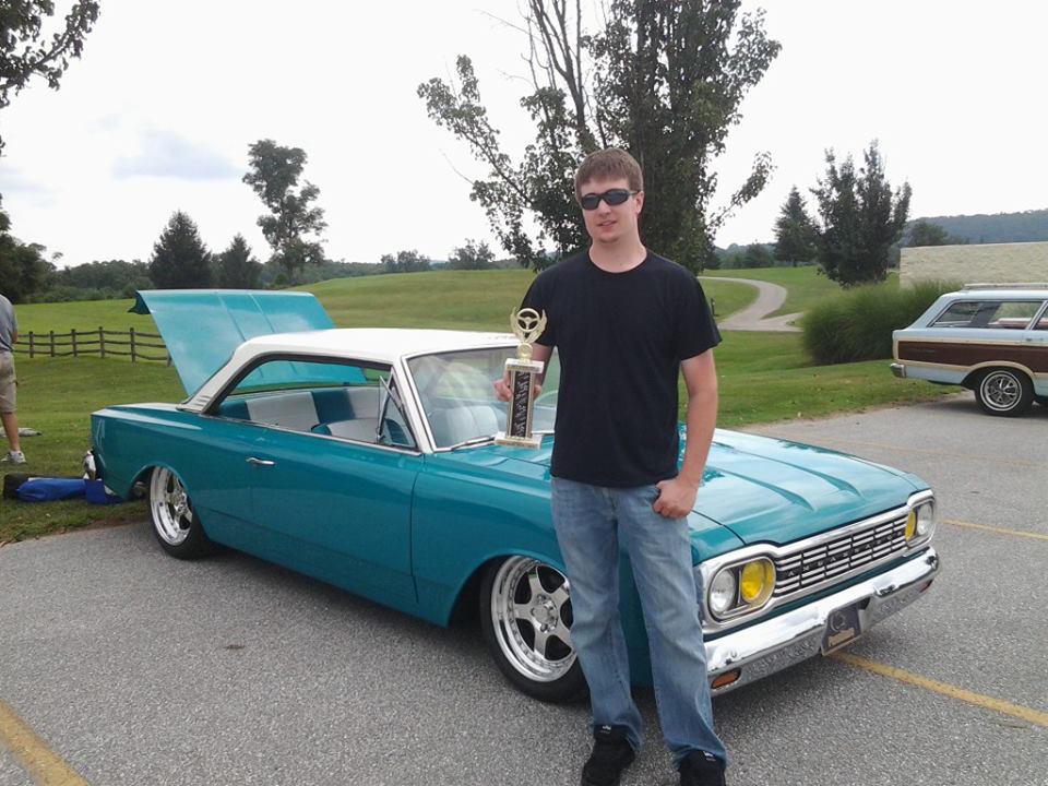 Man standing beside car holding trophy