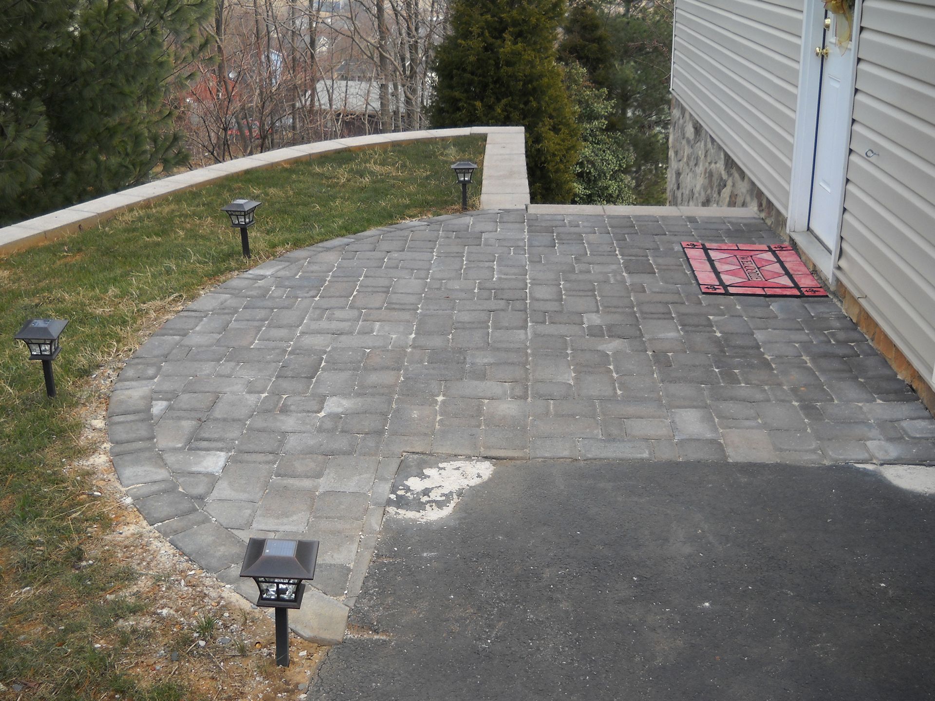 A brick walkway leading to a house with a red rug on the ground