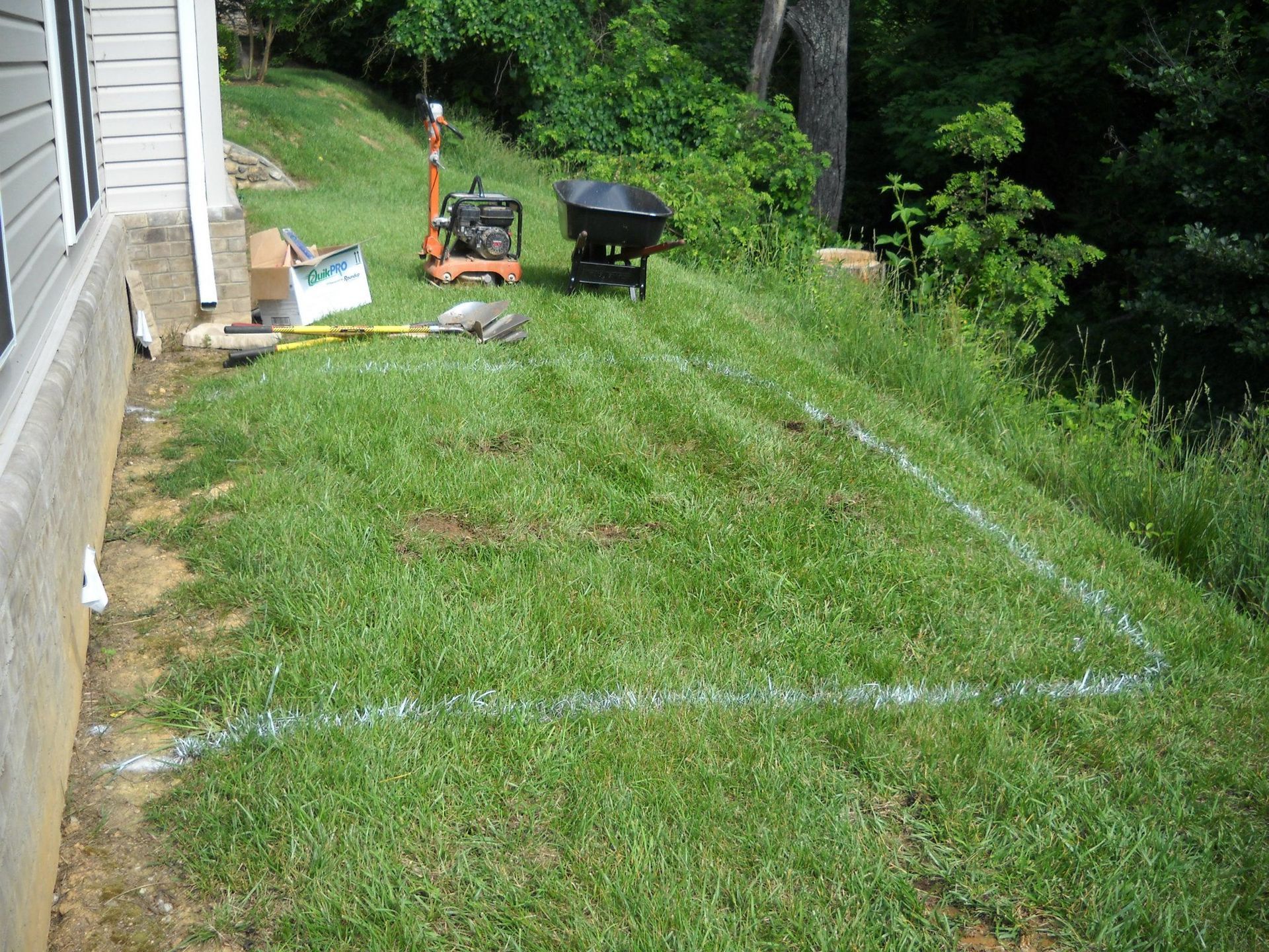 A wheelbarrow sits in the grass near a house