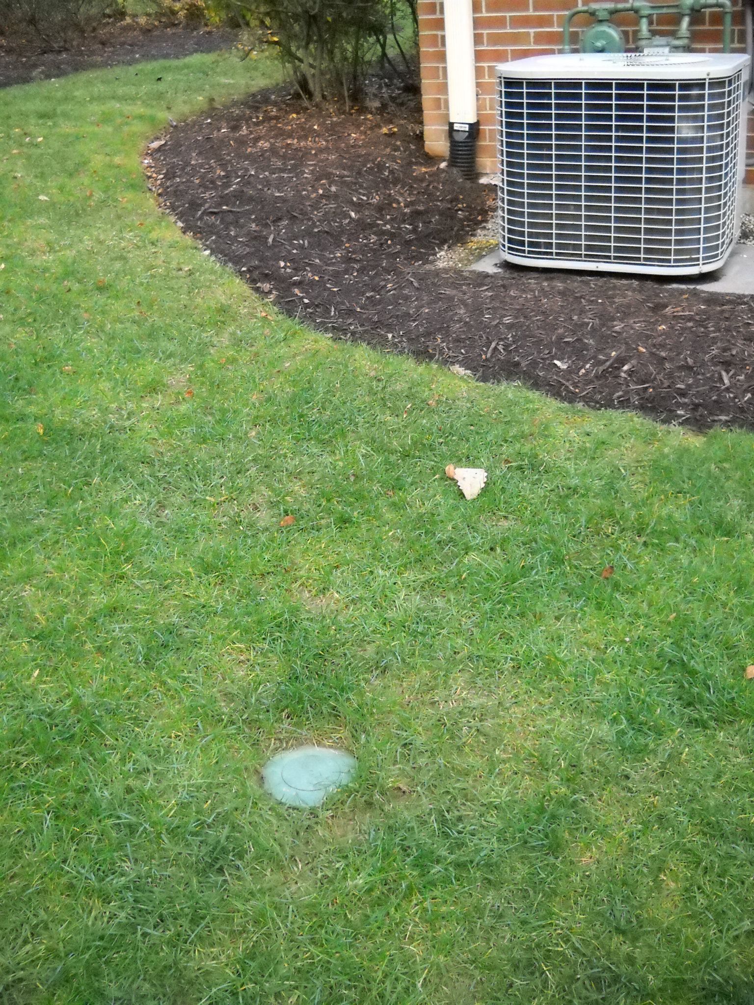 A lawn with a brick building in the background and a air conditioner in the grass.