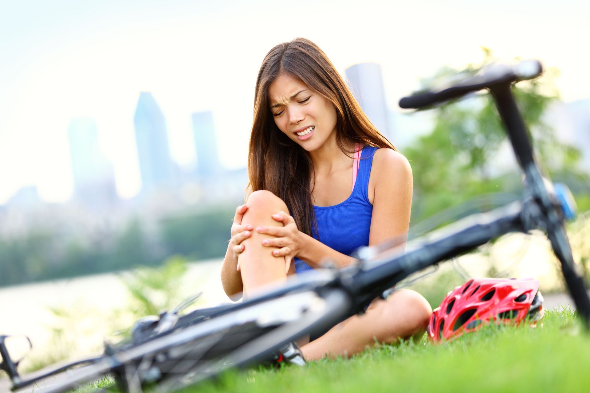 A woman is sitting next to a bicycle and holding her knee in pain.