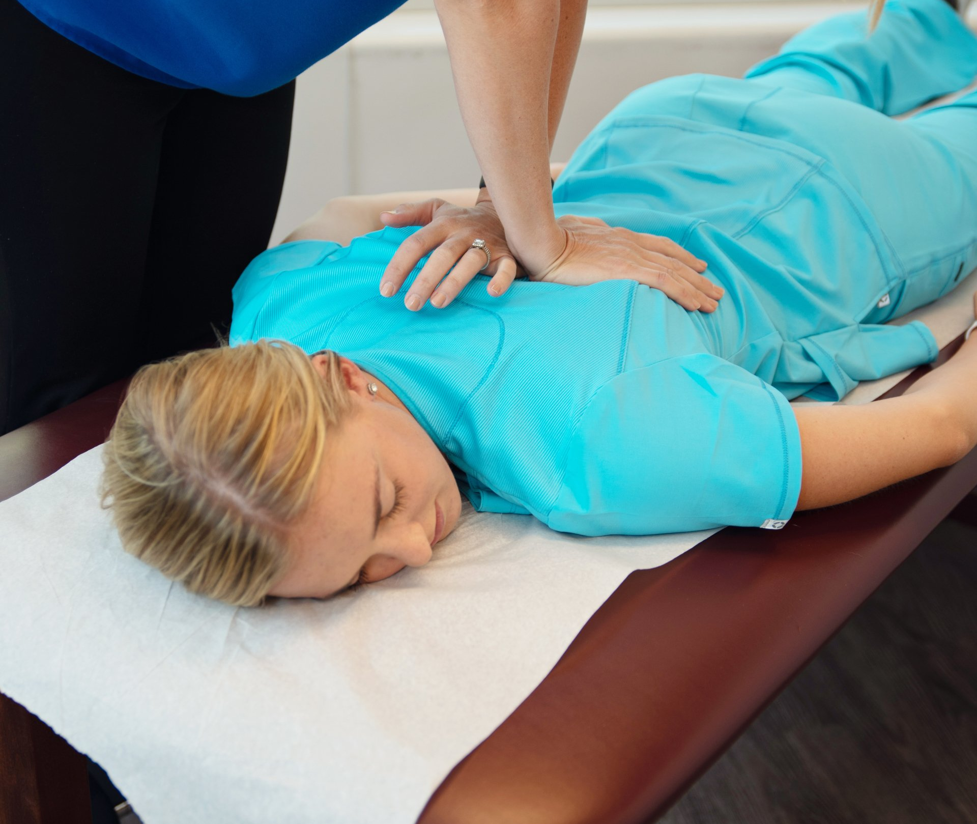 A woman in a blue scrub is laying on a table getting a massage.