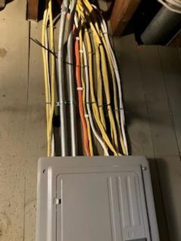 Electrical panel with multiple wires and conduit attached to a concrete wall.