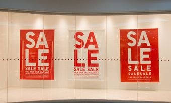 Three red sale signs are hanging on a glass wall.