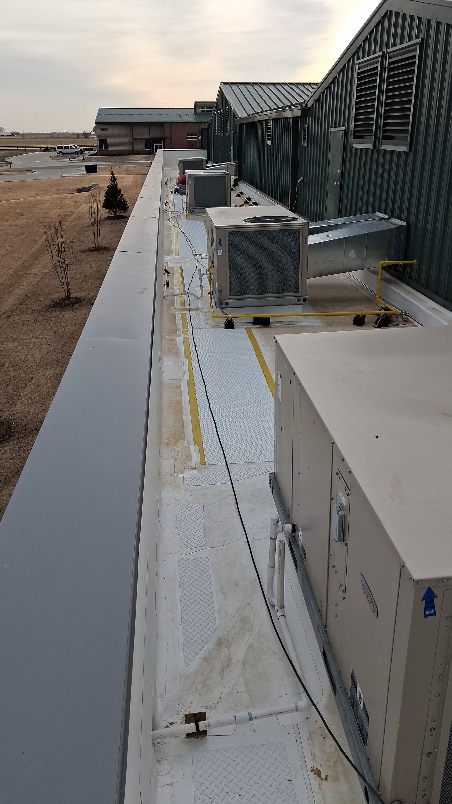 Rooftop HVAC units and ductwork along a flat roof beside a building under construction