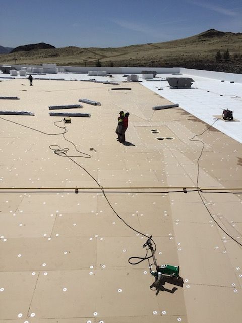 Workers install roofing membrane on a flat rooftop under a clear sky.
