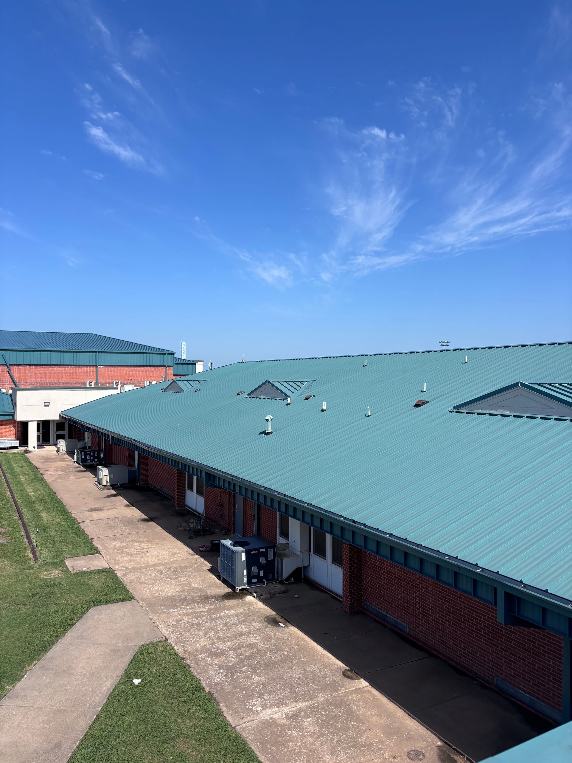 Brick school building with teal roof and walkway under a bright blue sky