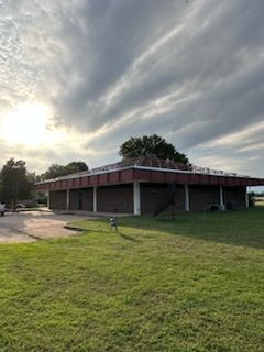 Low building with red roof on a grassy field under a cloudy sunset sky