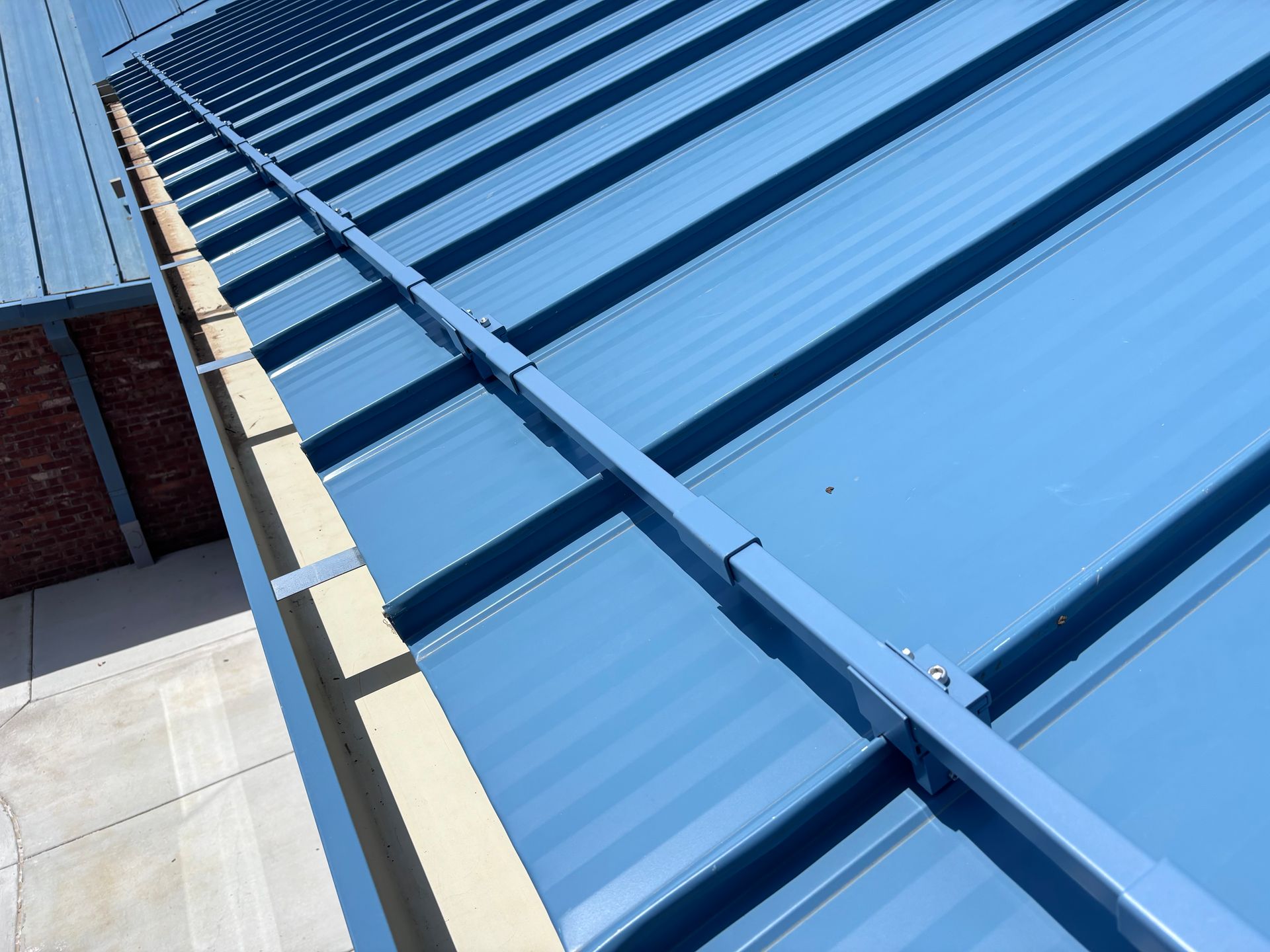 Blue metal roof panels with a row of beige trim along the edge beside a brick wall.