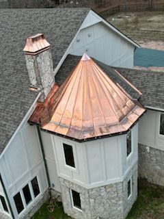 Aerial view of a stone house with a copper conical roof and chimney.
