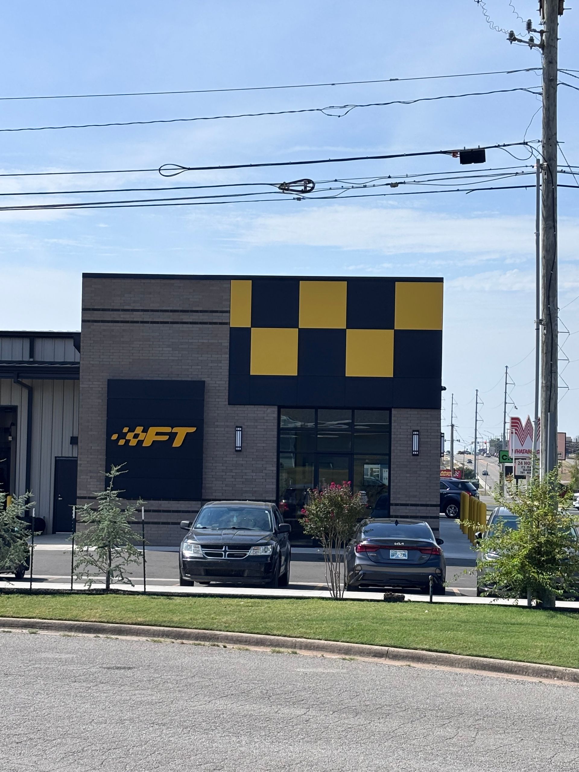 Dark building with yellow-and-black checkered facade, parked cars, and power lines under a blue sky