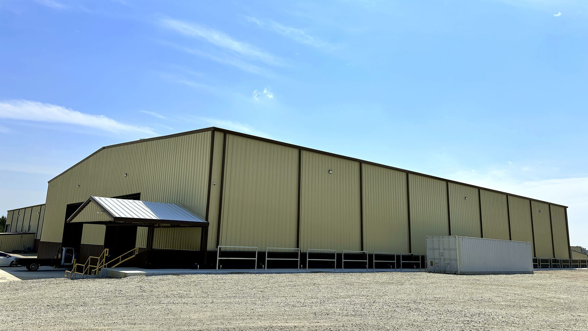 Large tan industrial warehouse tent on a gravel lot under a clear blue sky