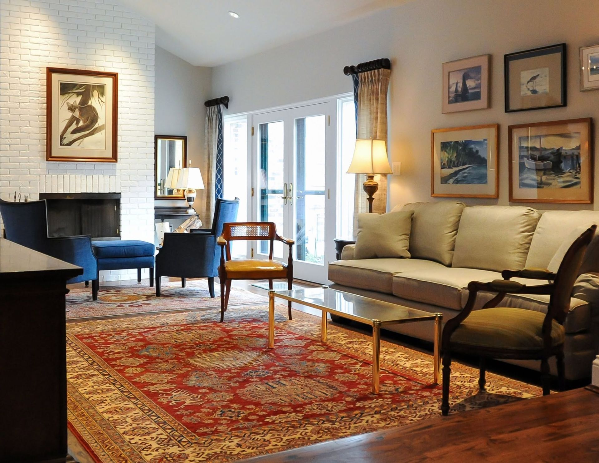 Cozy living room with beige sofa, blue chair, red rug, lamps, fireplace, and framed art on walls