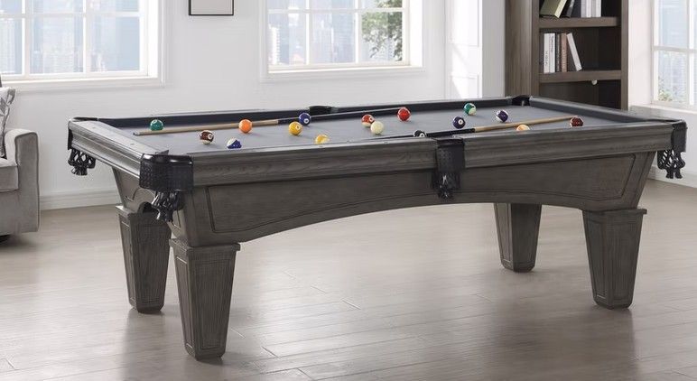 Gray pool table in a well-lit room with balls and cues arranged on it.