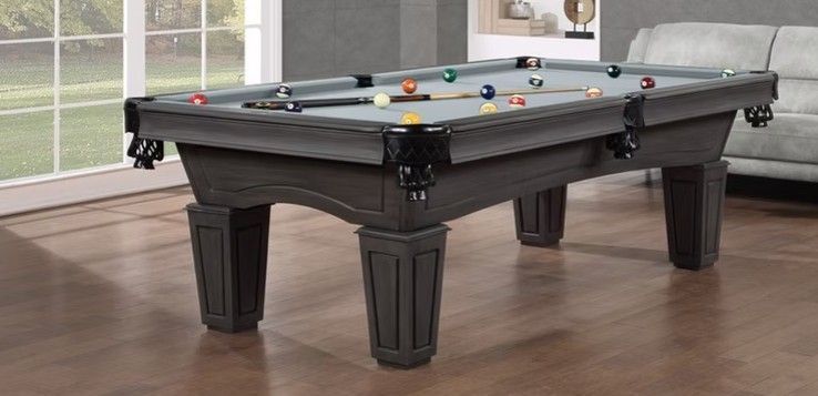 A gray pool table with pool balls on a hardwood floor.