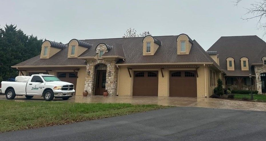 Suburban brick house with three garage doors, white pickup truck parked in front, and a wide driveway.