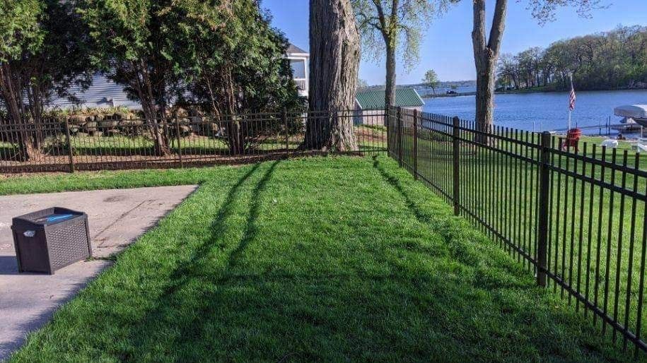A fence surrounds a lush green lawn next to a lake.