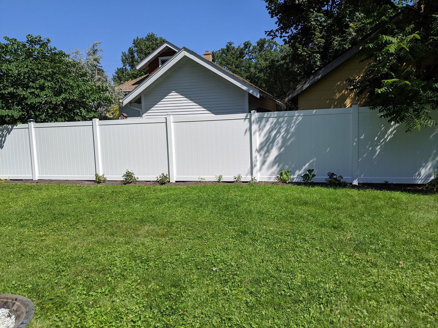 A white fence surrounds a lush green yard in front of a house.