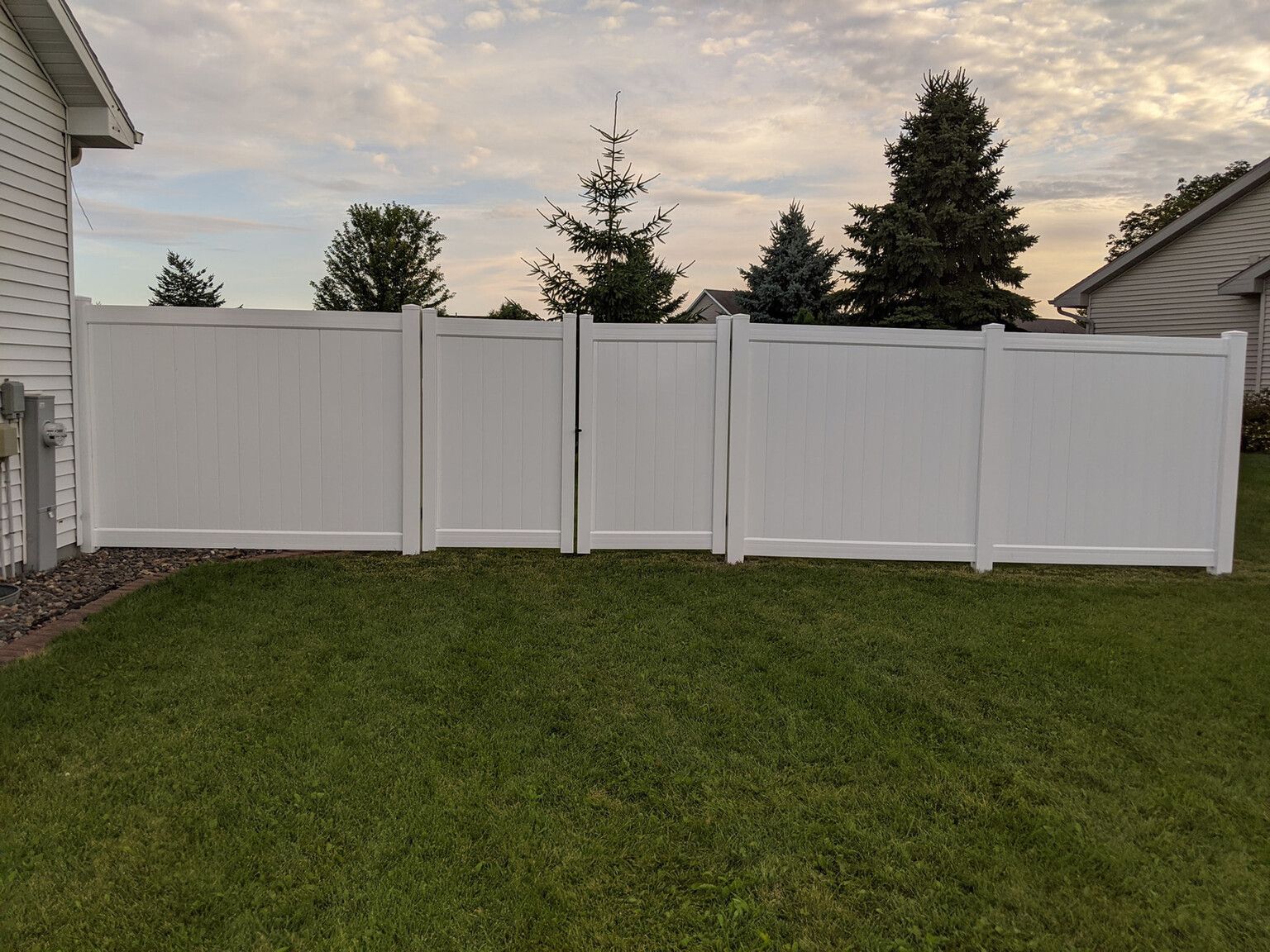 There is a white fence in the backyard of a house.