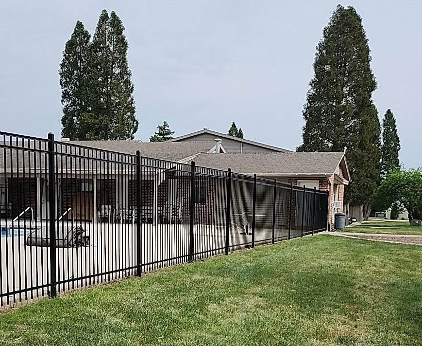 A black fence surrounds a swimming pool in front of a house.