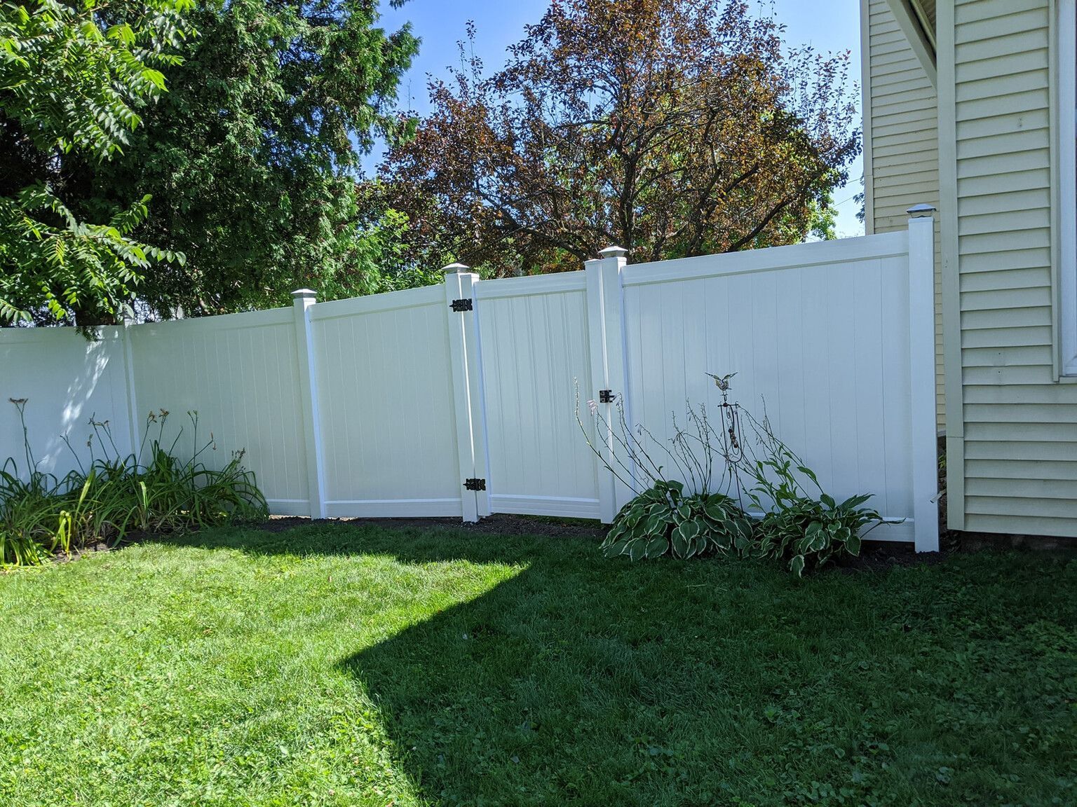 A white fence with a gate in the backyard of a house.