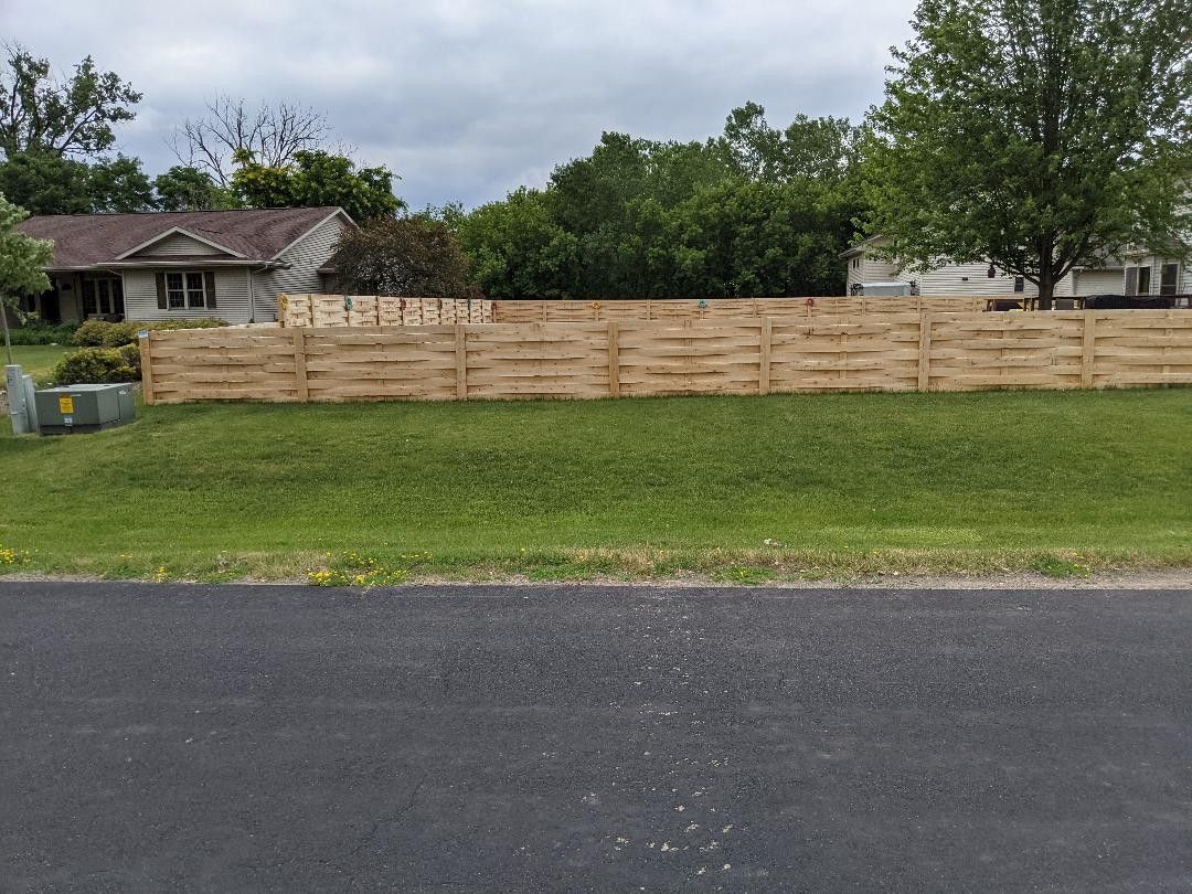A wooden fence surrounds a lush green field in front of a house.