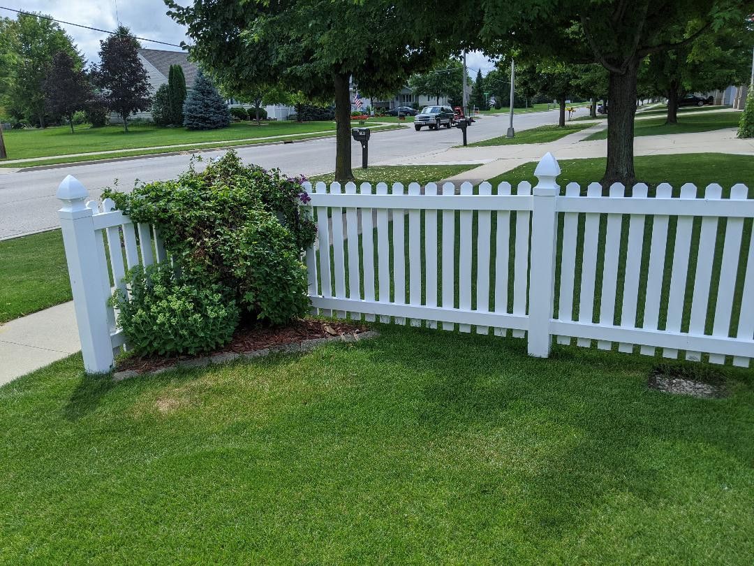 A white picket fence is in the middle of a lush green yard.