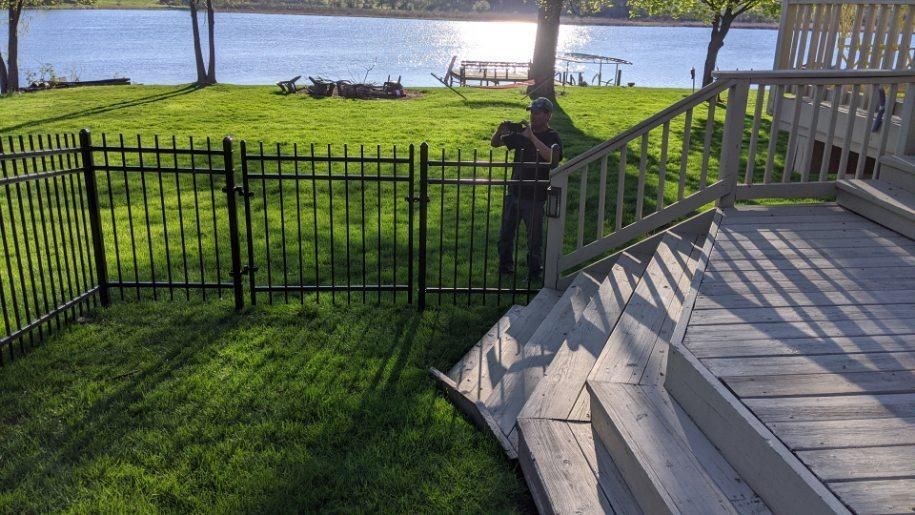 A man is standing on a deck next to a fence with a view of a lake.